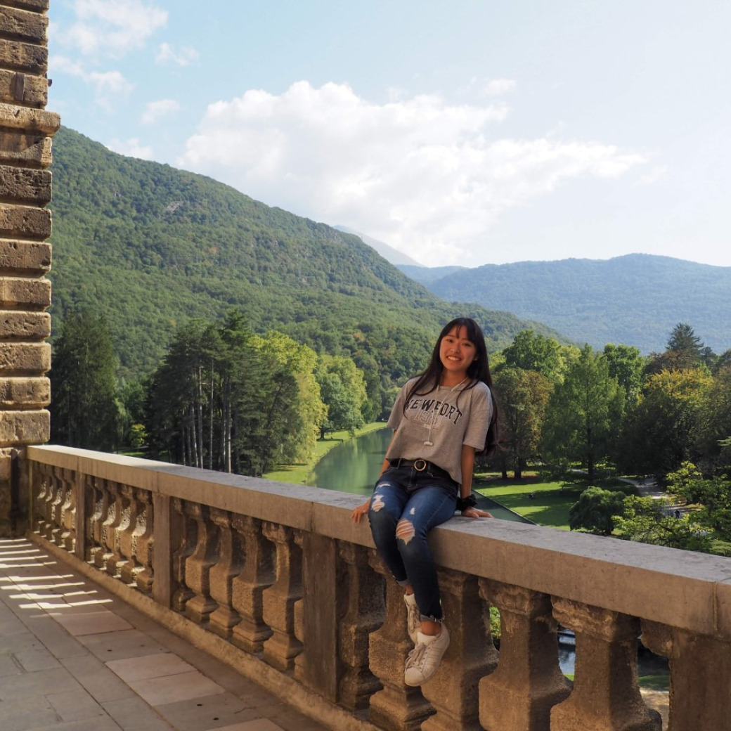 student sitting on ledge with green hills in background