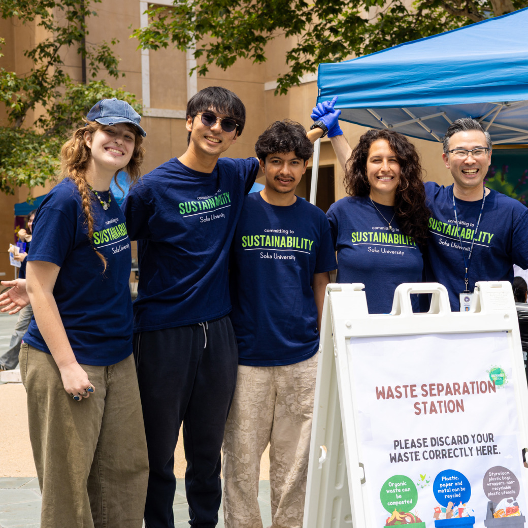 A group of four students and one staff member wearing matching navy t-shirts pose for a photo at their waste station, behind a sign instructing attendees.
