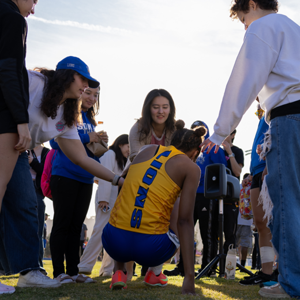 Friends lift up a Soka track athlete whose tank top reads "Lions" down the back.