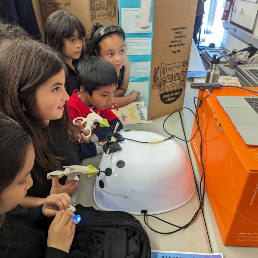 A group of children watching a laptop while a girl is using the machine