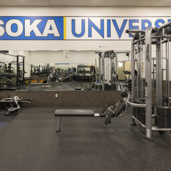 An empty weightroom with mirrors and "Soka University" written in all caps on the wall.