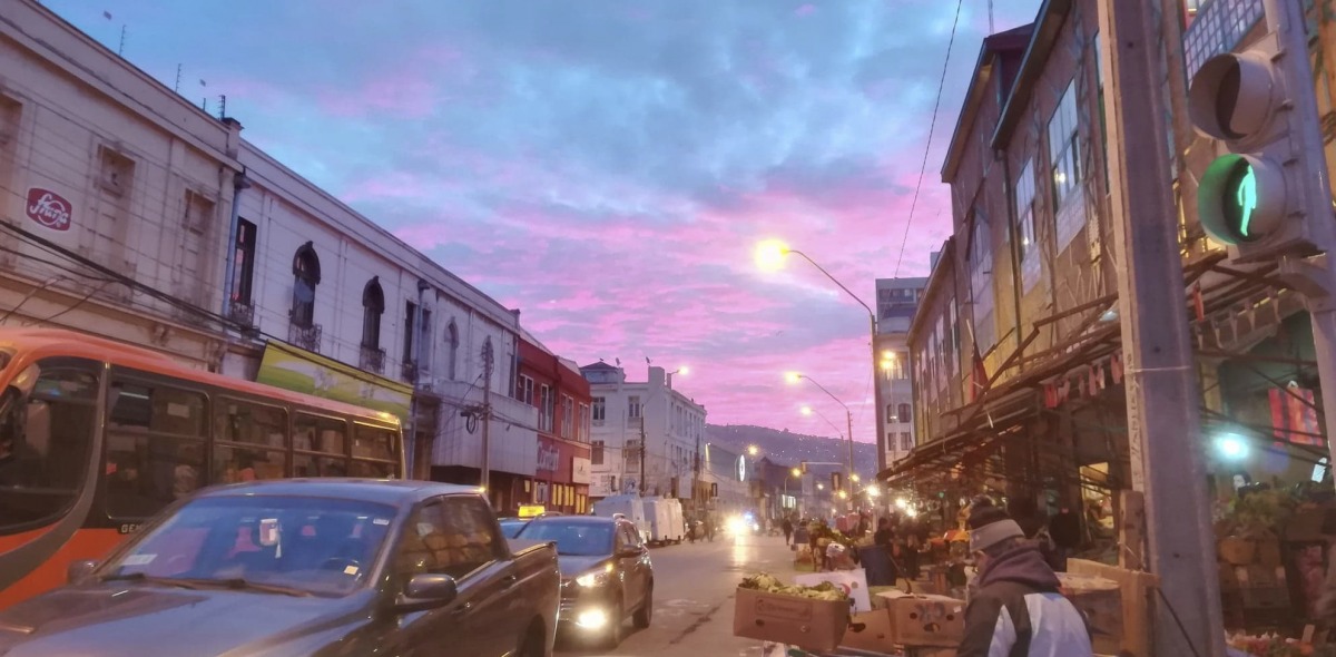 A picture of a Chilean street during sunset with cars passing by and street vendors lining the road.