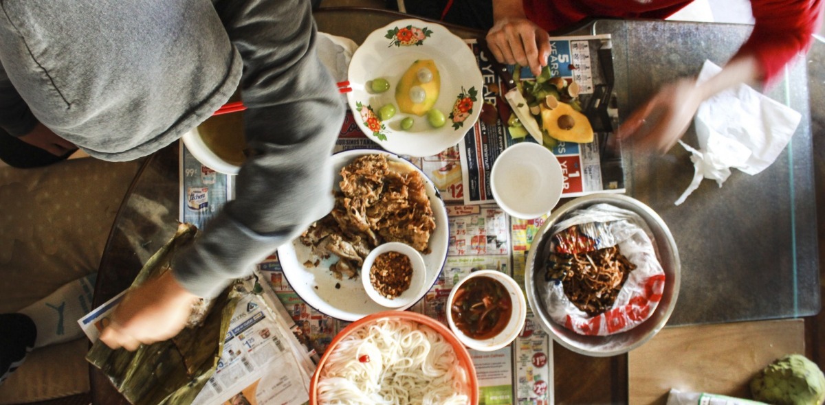 An overhead picture of a table covered by food and surrounded by people. 