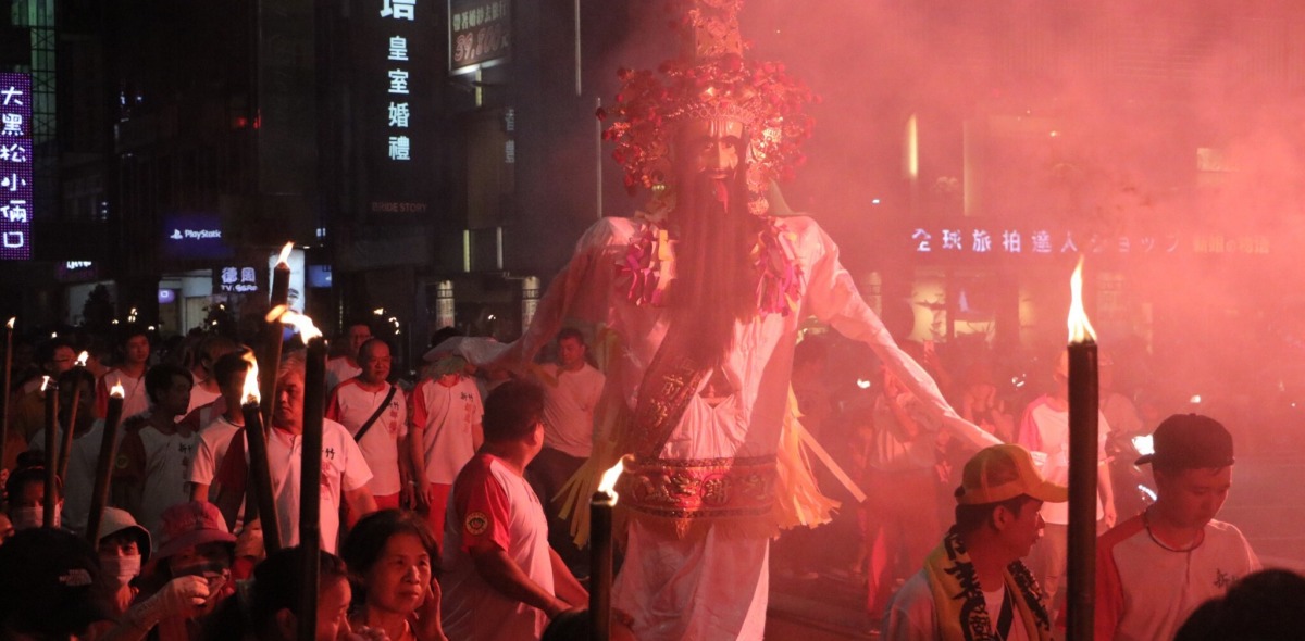 An effigy of a deity illuminated by red light is marched through the streets at night.