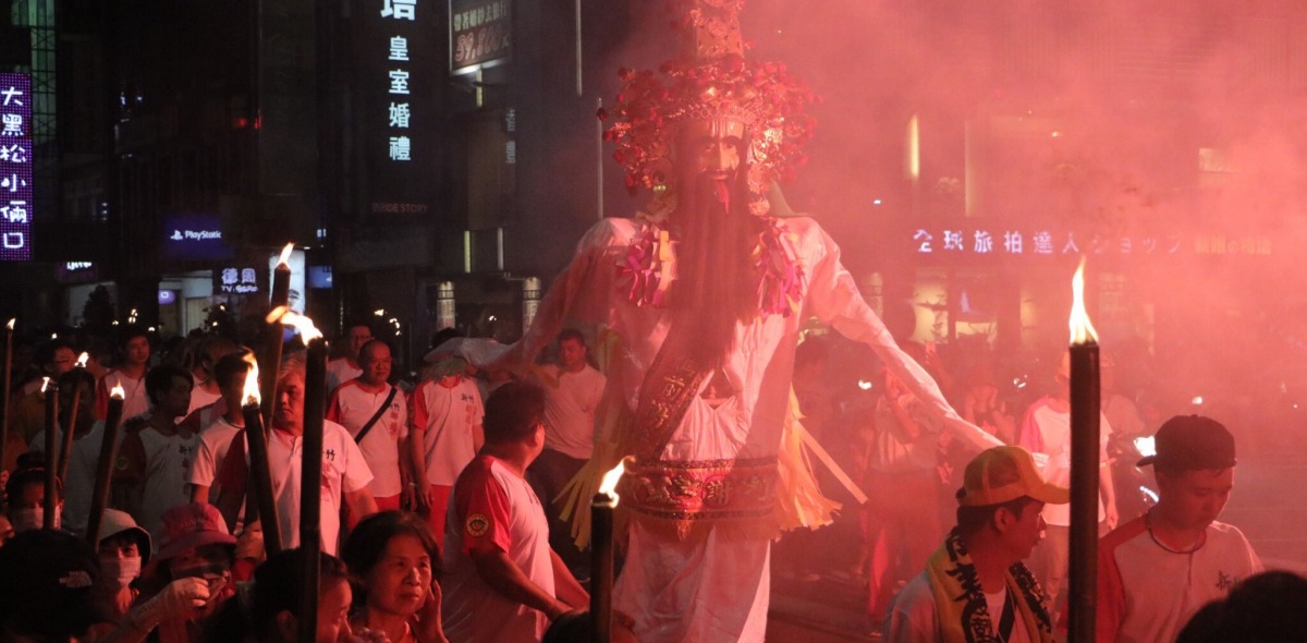 An effigy of a deity illuminated by red light is marched through the streets at night.