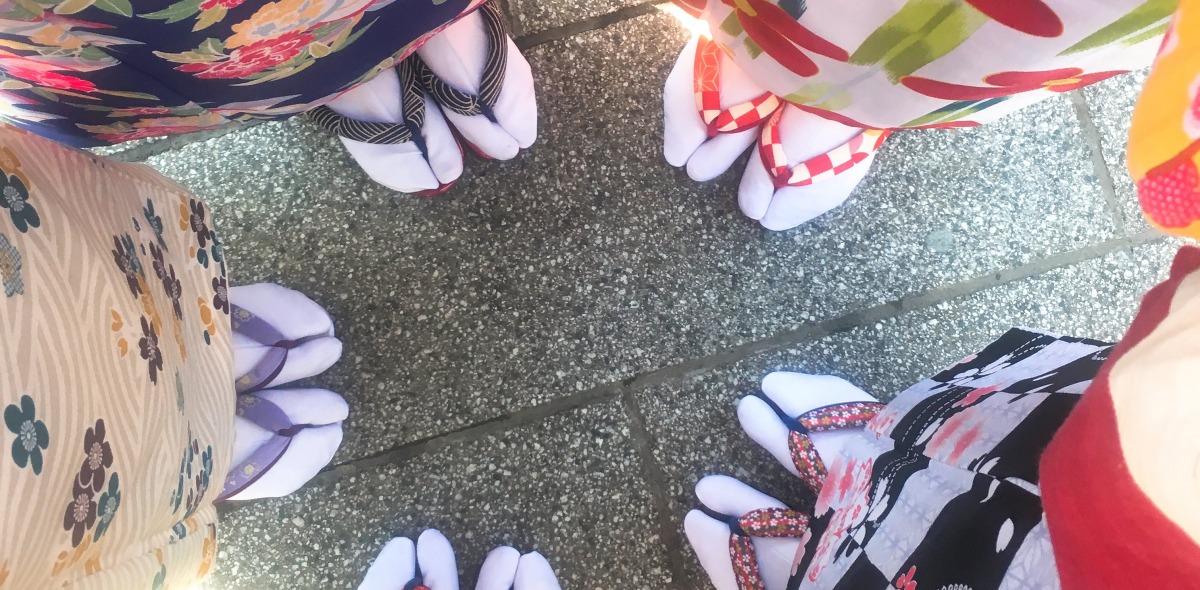 An overhead shot of five people's feet facing together, dressed in traditional Japanese sandals and kimonos. 