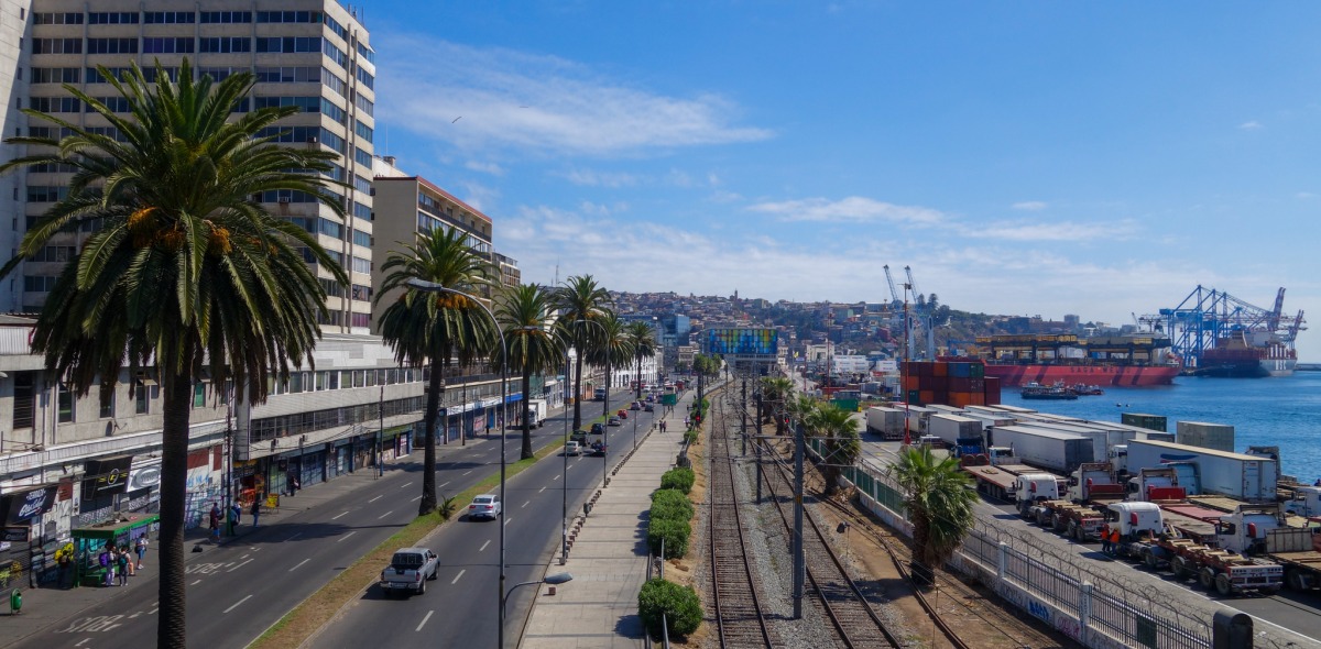 A picture of a railroad running alongside the ocean with commercial buildings rising to the side. 