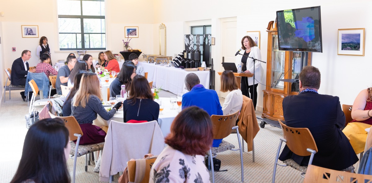 Image of speaker addressing a group of people seated at tables.