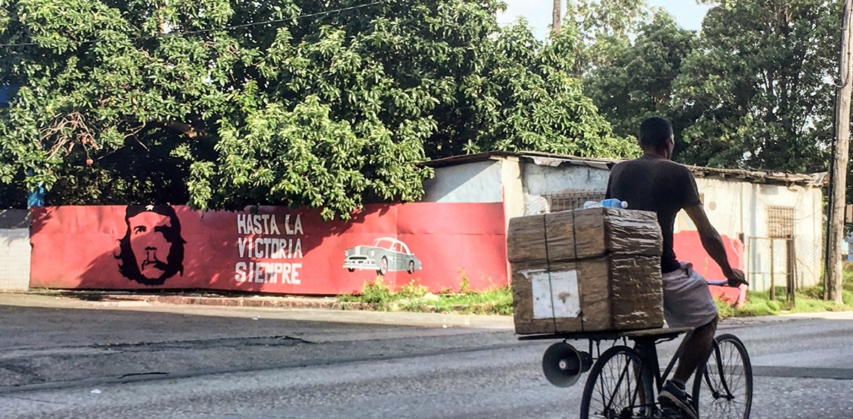 A man biking past a mural on a wall reading "Is Victory Freedom?" in Spanish. 