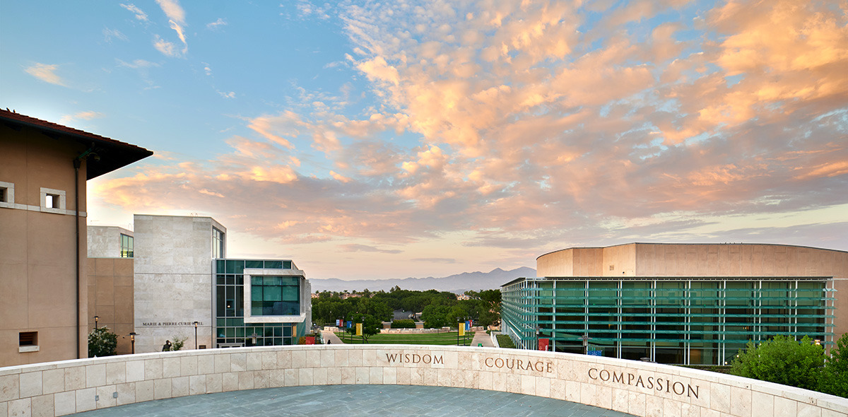 Central values of Soka University, Wisdom, Courage, and Compassion displayed on a wall in front of clouds and silhouetted mountains in the background