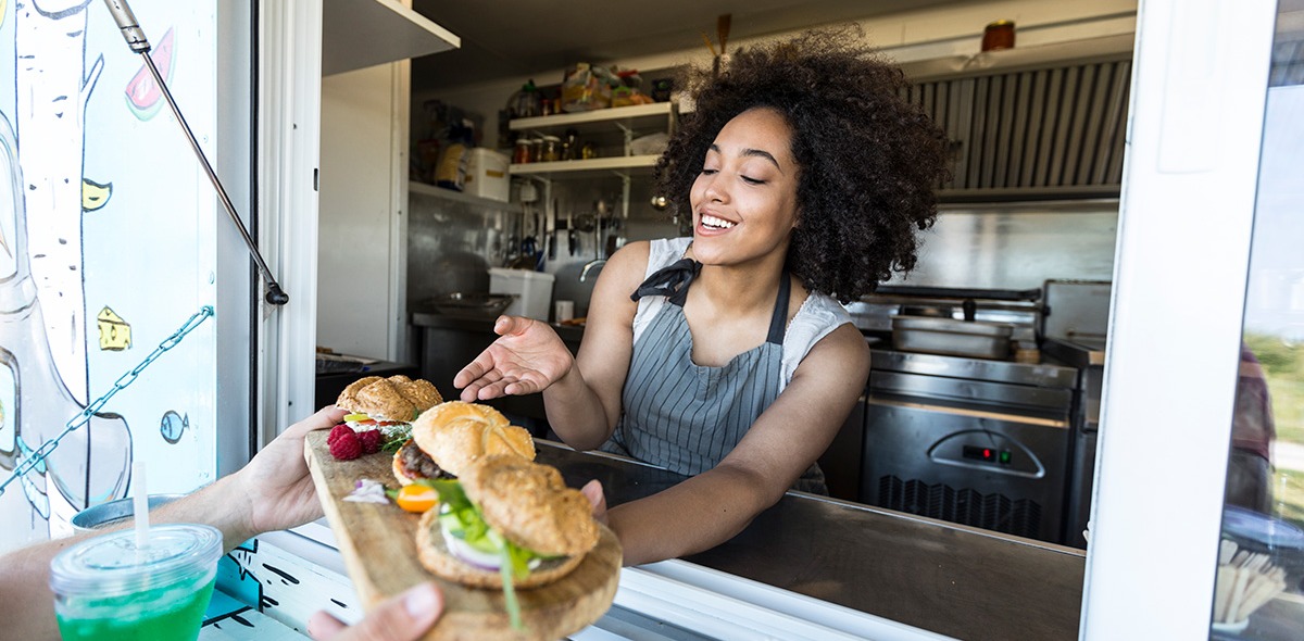 Food truck employee serving burgers to customer's hands