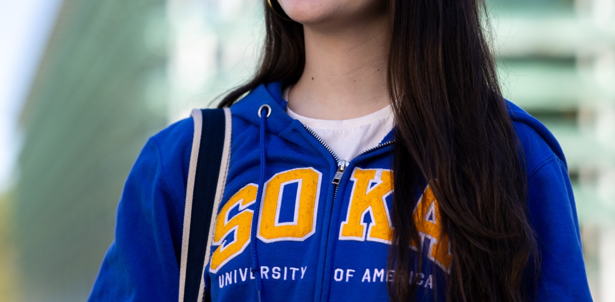 Valentina Ferreira Einsfeld '26 wears a blue hoodie that says "Soka" in yellow lettering and she smiles off into the distance on SUA's campus.