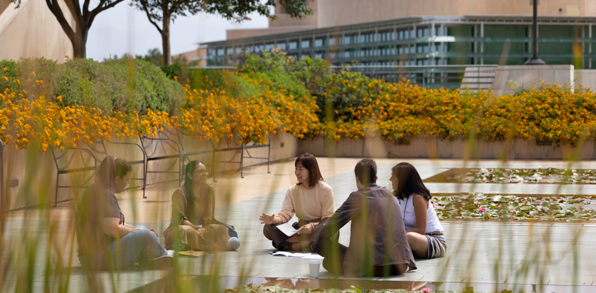 Five people sit on the ground in a circle by the lily ponds on SUA's campus.