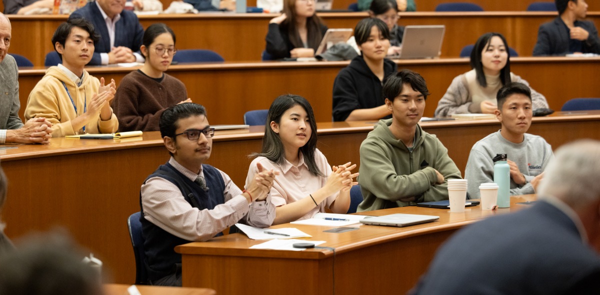 Students clap for a speaker in a large auditorium.