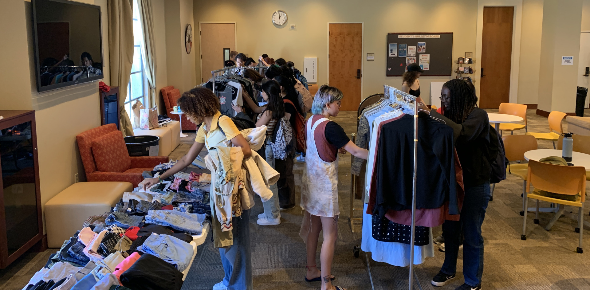 Students participate in a clothing swap event browsing racks and piles of clothing.