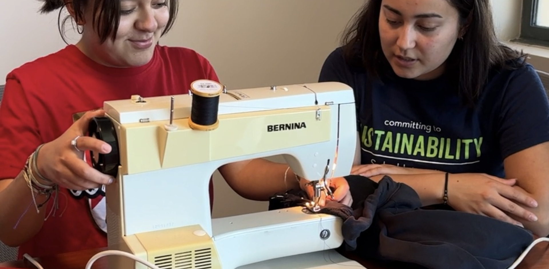 Two students use a sewing machine during a mending workshop.