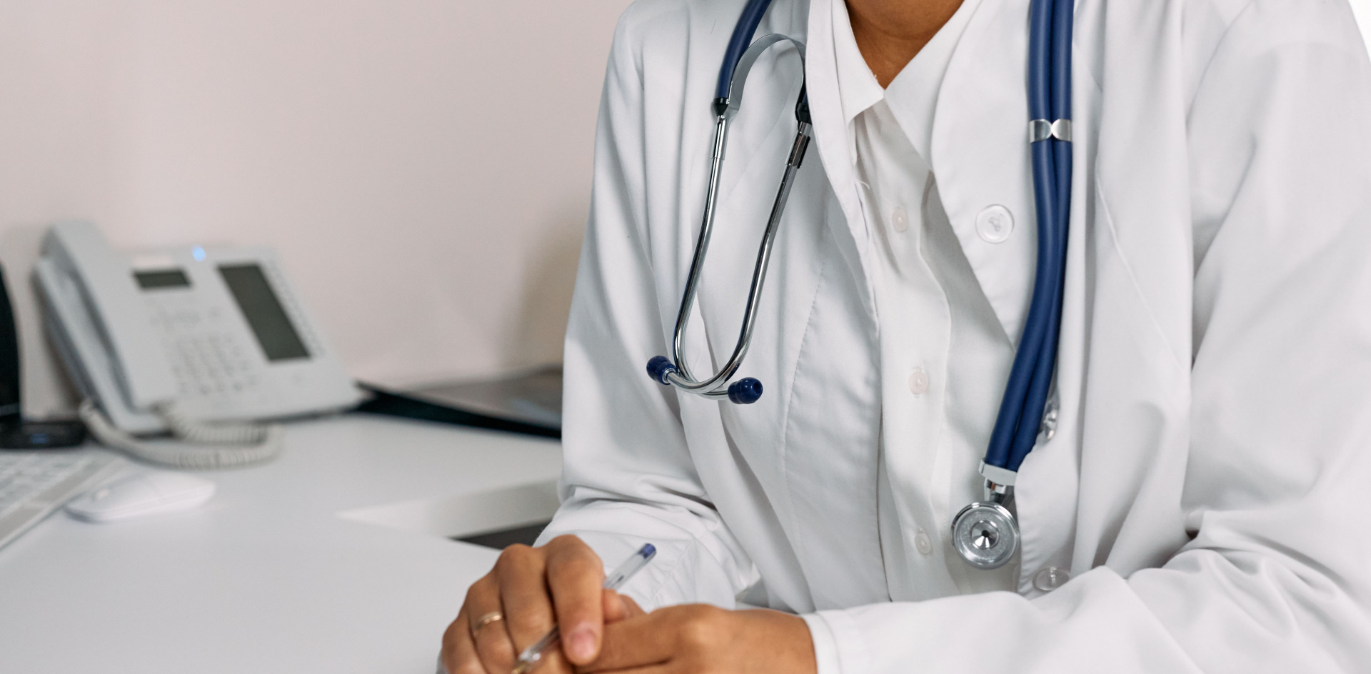 Doctor with stethoscope and white coat seated at a clinic desk