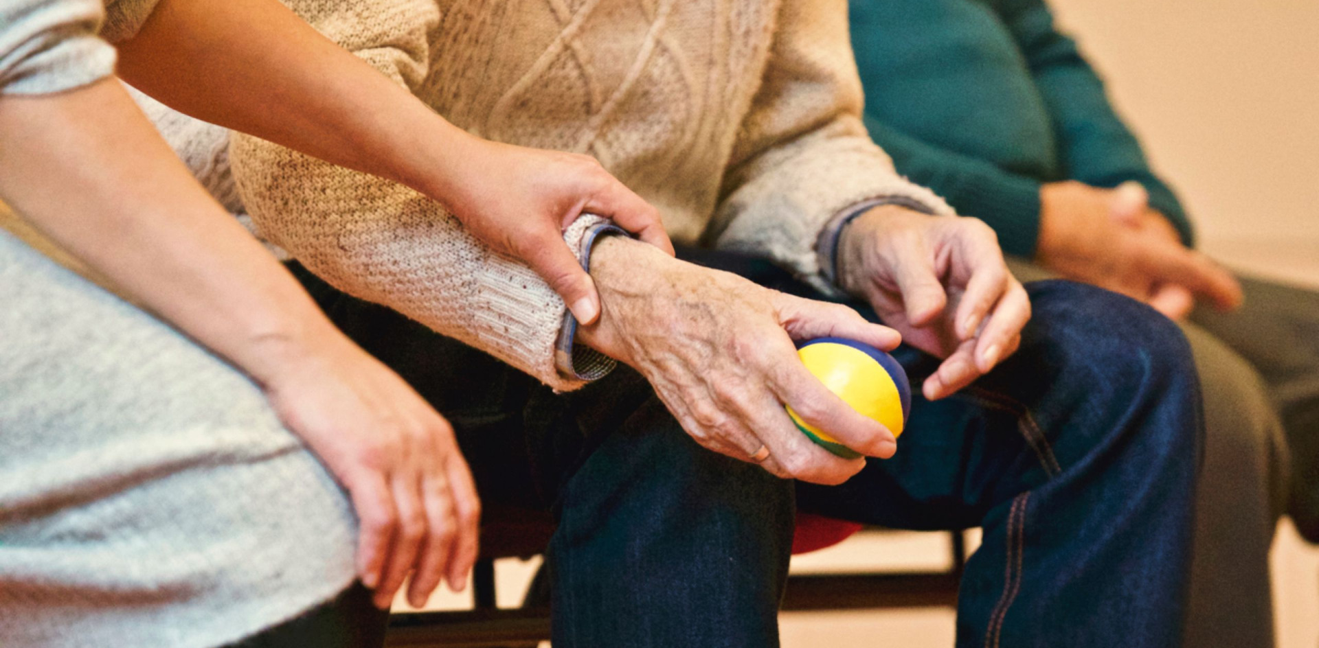 An elderly person receives support from an OT with a ball to hold in hand 