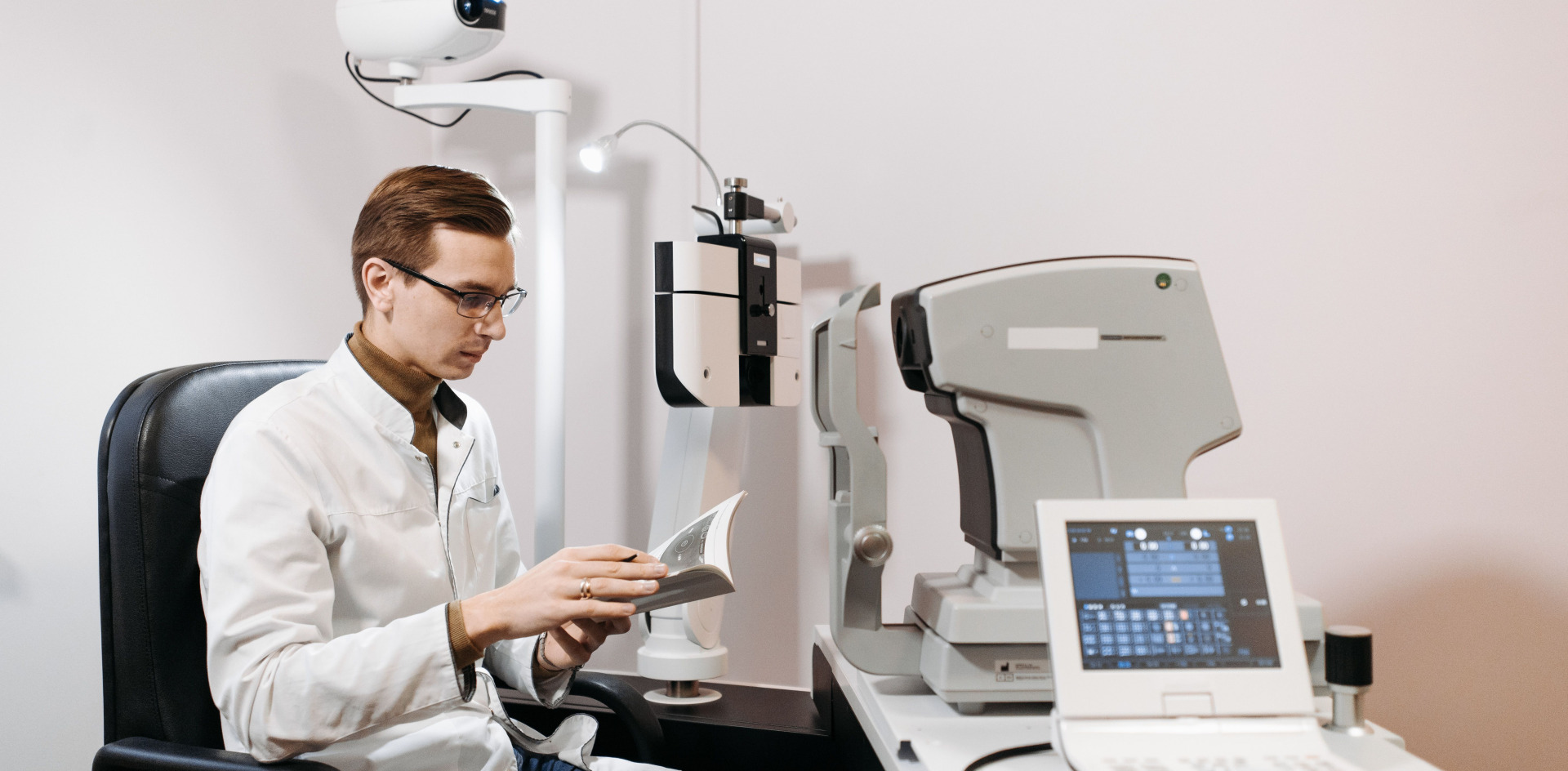 Optomist in clinic using ophthalmology equipment, wearing glasses and a lab coat, reviewing documents