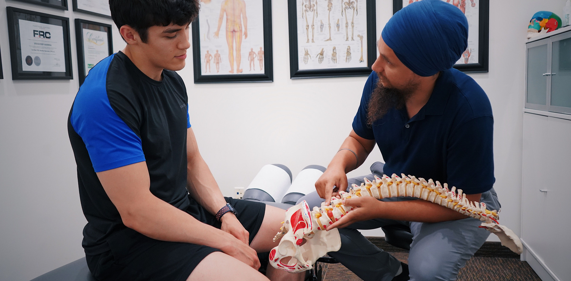A PT explaining spinal issues to a patient using a spine model during a medical consultation