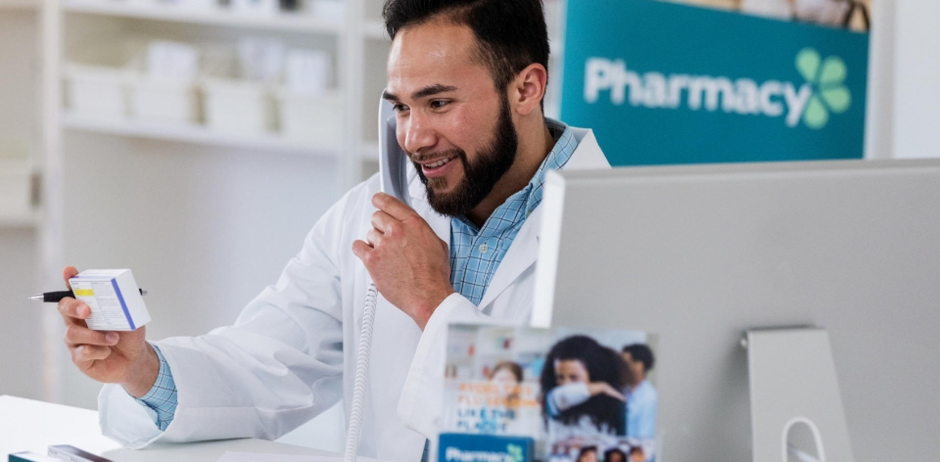 A pharmarcist on the phone call, sitting in a pharmacy setting