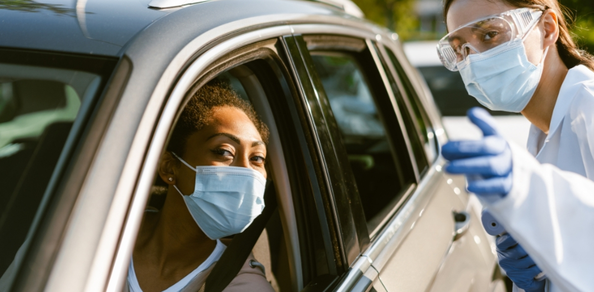A women in white blouse, wearing glasses and facemask providing instructions for a car driver