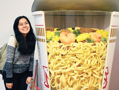Student stands in front of life-size Cup of Noodles statue