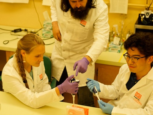 Two students with a professor in a lab. 