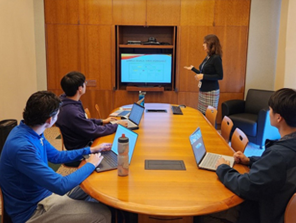 Librarian Jenn Tirrell leads a workshop in the Library with students sitting at a round table, looking at a screen.