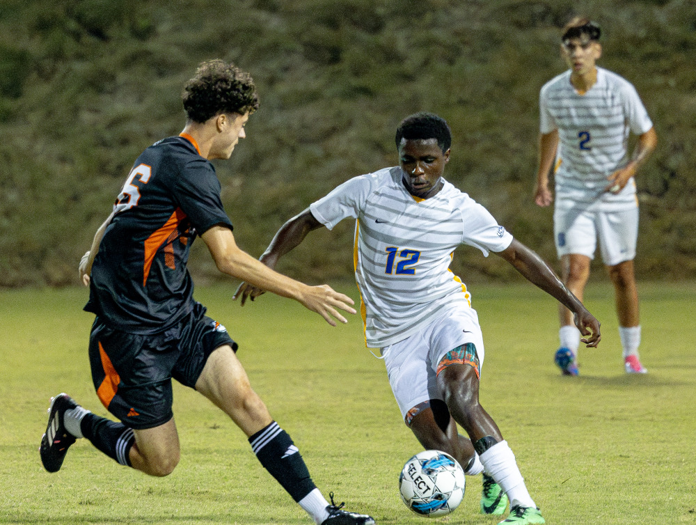The Soka soccer team in white is competing with another school and one of them is about to hit the ball