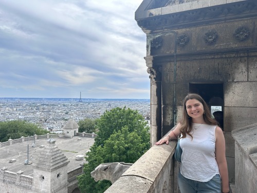 A girl poses at an overlook with the Eiffel Tower in the distance