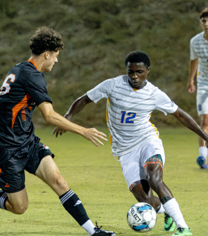 The Soka soccer team in white is competing with another school and one of them is about to hit the ball
