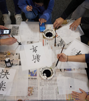Overhead shot of students gathered around a table practicing Chinese calligraphy.