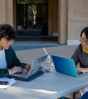 Two students sitting outside the library, working on their laptops