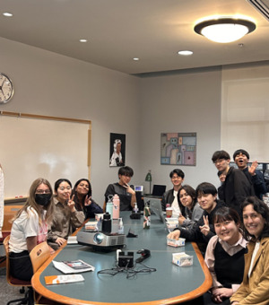 Many students are gathered around a large table smiling at the camera. 
