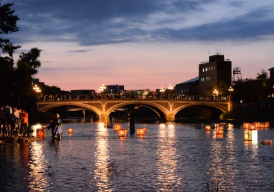 Picture of a bridge illuminated from behind by a sunset and underneath by lanterns floating on the water.