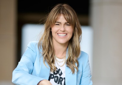 Erica Baldaray poses outside wearing a powder blue blazer over a white t-shirt that says "Go Sports" for the Women of SUA photoshoot