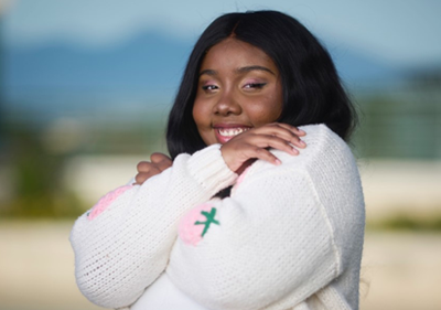 Sasha Woods smiles and hugs herself as she poses outside on Soka's Campus