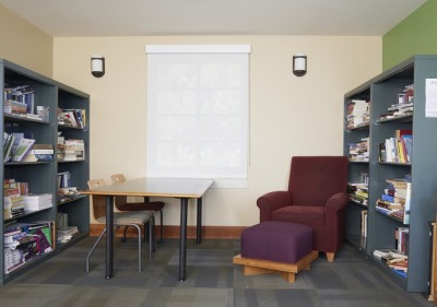 a room with 2 bookshelves on opposing sides of the room with a table and maroon sofa chair in the middle. 