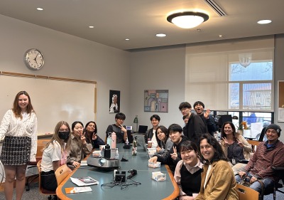 Many students are gathered around a large table smiling at the camera. 