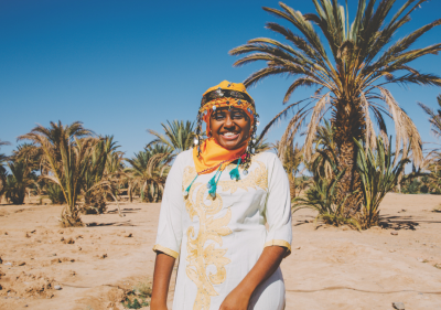 A woman smiles while wearing traditional garb in a desert. 