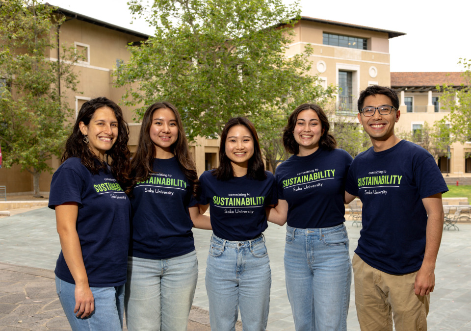 5 students wearing matching navy shirts that says "sustainability" pose for a photo outside on SUA's campus.
