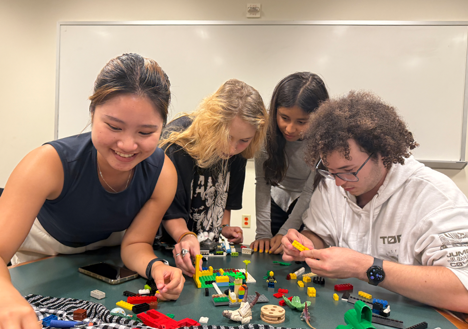 Four students work with legos on top of a green table to practice urban planning.