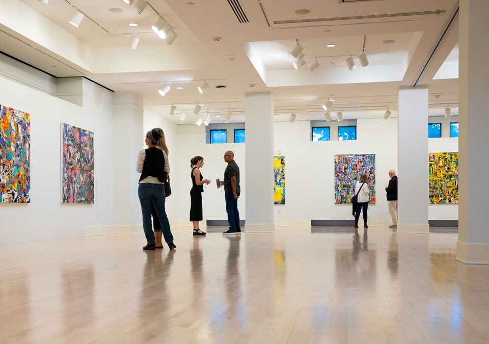 People look at art in a gallery and mingle amongst themselves.