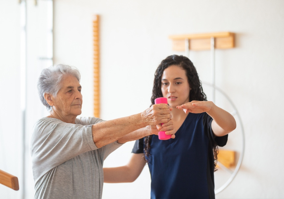 An OT helping an elderly woman lifting a light weight
