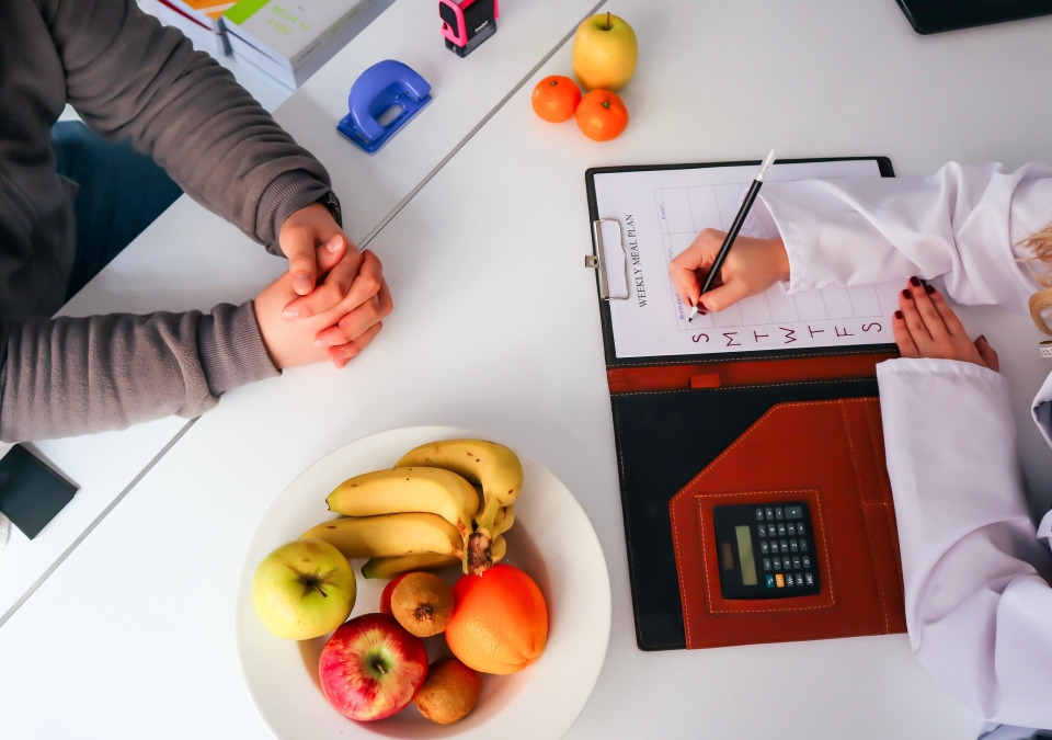 A doctor taking note on patient records, next to a fruit dish on the clinic desk