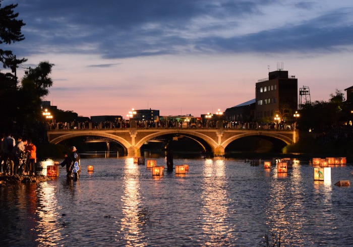 Picture of a bridge illuminated from behind by a sunset and underneath by lanterns floating on the water.