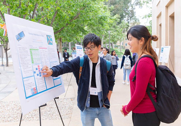 Students discuss findings at an easel displaying a poster