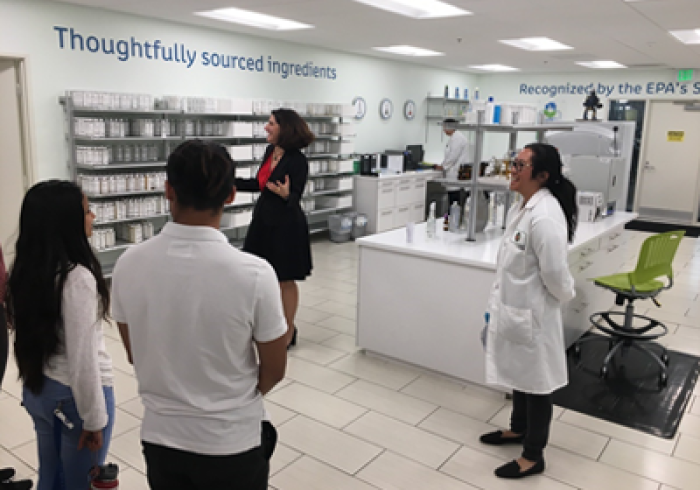 Students stand in a science lab and listen to a woman speaking