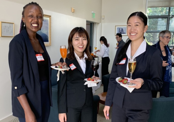 Three women hold plates and glasses during an etiquette training